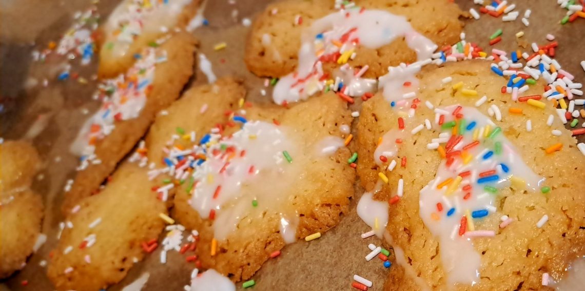 Kekse mit Zuckerguss und bunten Zuckerstreuseln auf einem Backblech