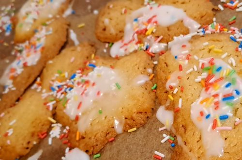 Kekse mit Zuckerguss und bunten Zuckerstreuseln auf einem Backblech